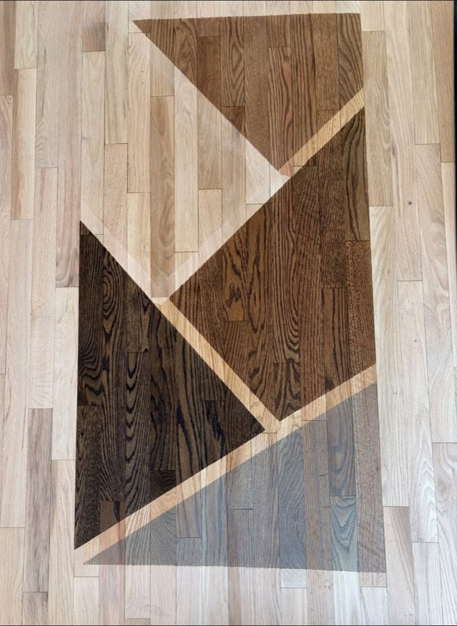 A sample panel of four different stain tones laid out in geometric blocks on a freshly sanded raw red oak floor.